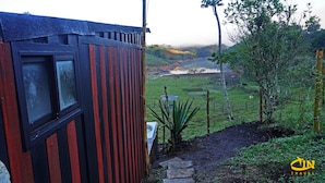 A rustic cabin with a window, a view of a green landscape, and a distant body of water. - Hotel Selva Negra (Guatapé)