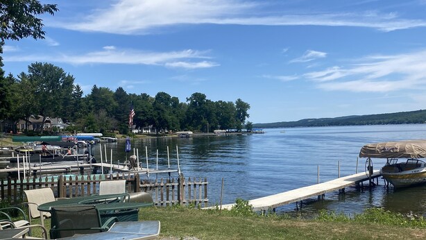 A lakeside patio with outdoor seating and a dock extending into the water. - Remodeled beautiful farmhouse with stunning lake view (Honeoye)