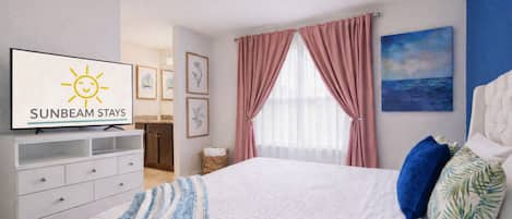 A bedroom with a bed, a television displaying 'SUNBEAM STAYS,' a ceiling fan, and a painting on the wall.