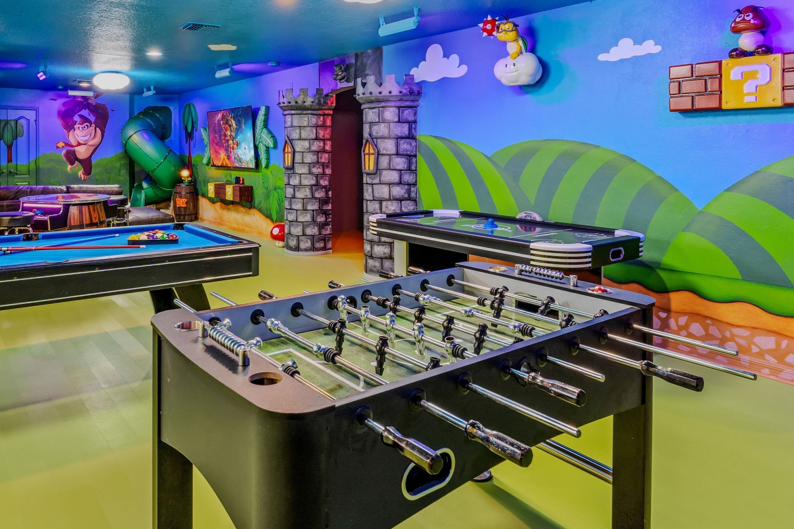 A room with two foosball tables, a pool table, and a dartboard.