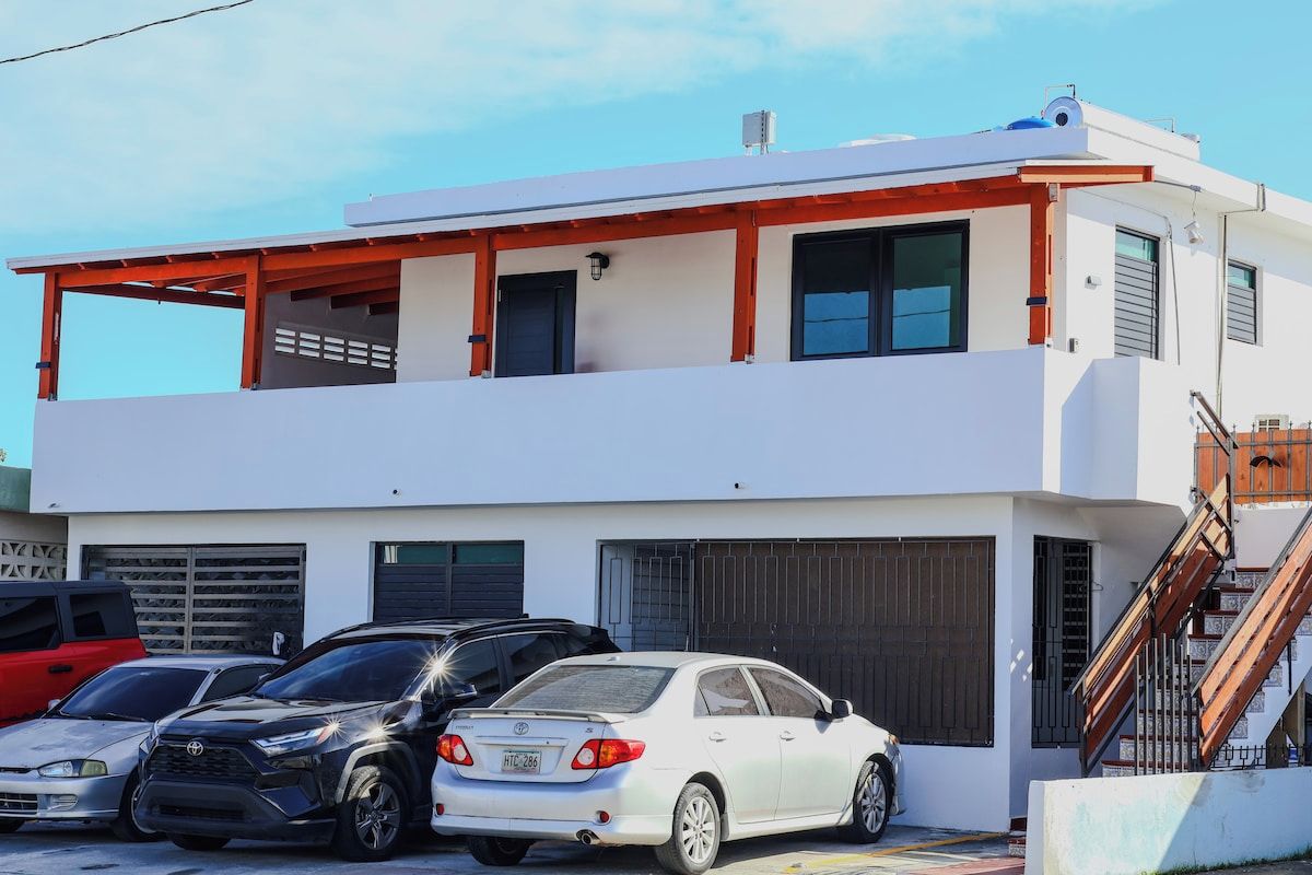 Un edificio de dos plantas con garaje, coches estacionados y una escalera que lleva al nivel superior.