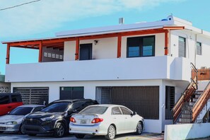 Un edificio de dos plantas con garaje, coches estacionados y una escalera que lleva al nivel superior.