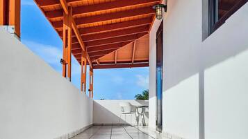 Un corredor techado al aire libre con suelo de baldosas, vigas de madera y vistas al cielo.