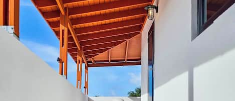 A covered outdoor corridor with a tiled floor, wooden beams, and a view of the sky.