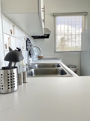 A modern kitchen with a stainless steel sink, a range hood, and a window with decorative bars.