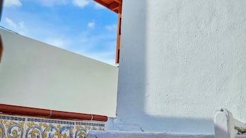 Un espacio al aire libre techado, con techo de madera, pared blanca con dispositivo de seguridad y piso de baldosas con diseño decorativo.