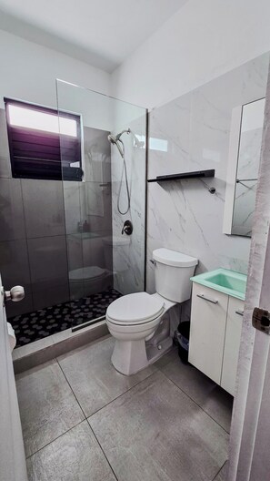 Un baño moderno con ducha envuelta en vidrio, inodoro e lavabo con encimera de mármol.