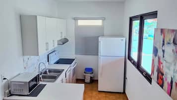 Cocina compacta con lavamanos, estufa y refrigerador, un pequeño comedor con una silla y una ventana con vistas.