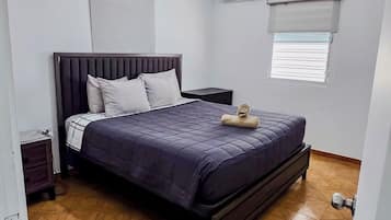 A bedroom with a bed, a nightstand, a window with blinds, and a ceiling light.