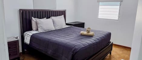 Un dormitorio con una cama, una mesita de noche, una ventana con persianas y una lámpara en el techo.