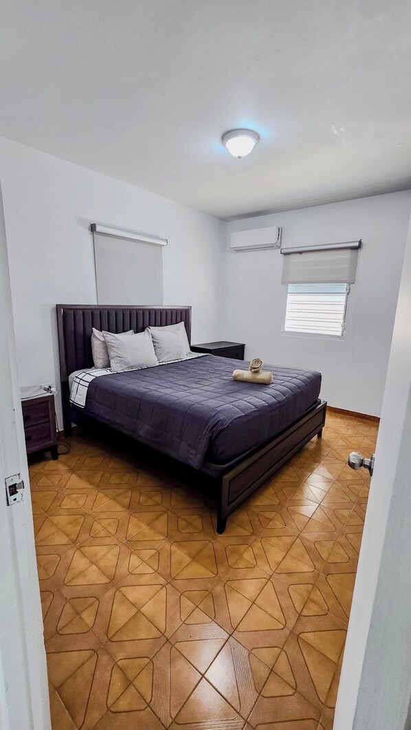 A bedroom with a bed, a nightstand, a window with blinds, and a ceiling light.