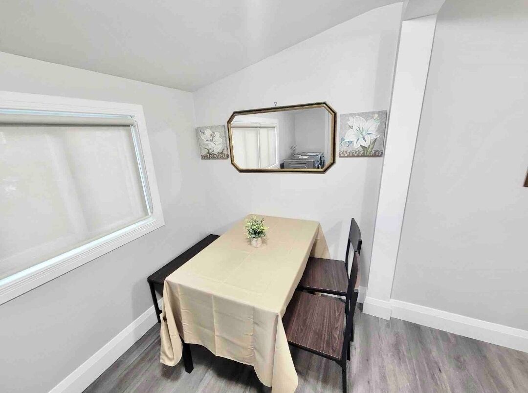 Ein Essbereich mit Tisch, Stühlen, einem Fenster und einem Spiegel an der Wand.