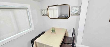Ein Essbereich mit Tisch, Stühlen, einem Fenster und einem Spiegel an der Wand.