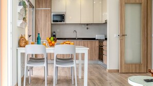 A modern kitchen with white cabinets, a microwave, and a sink. There is a dining table with two chairs and a fruit bowl. - Bright Apartment with Pool in Portimão | 5 Min Walk to the Beach by Lisbeyond (Portimão)