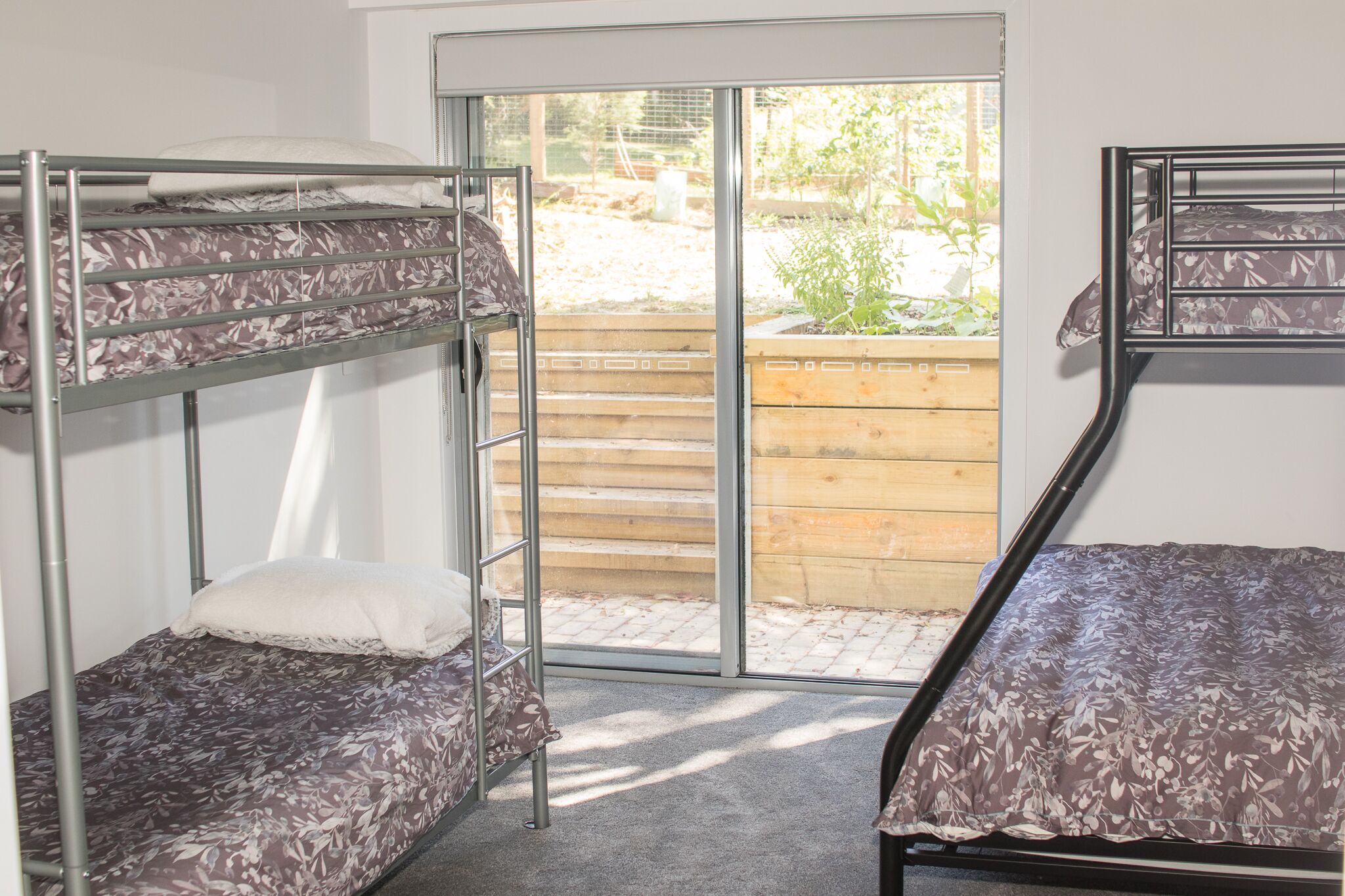 Una habitació de dormitori amb literes, una porta corredissa de vidre que dona a una zona exterior i una tanca de fusta visible a través de la porta.
