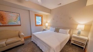 A bedroom with a large bed, a nightstand, a lamp, a window, and a map on the wall. - Beachy OBX 2Bedrm-No Stairs-Close to beach and shops! (Kill Devil Hills)