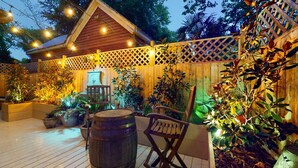 Un espacio al aire libre con patio de madera, cerca de madera y luces colgantes.