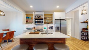 Una cocina moderna con armarios blancos, una isla central con taburetes, un microondas, un refrigerador y una cafetera.