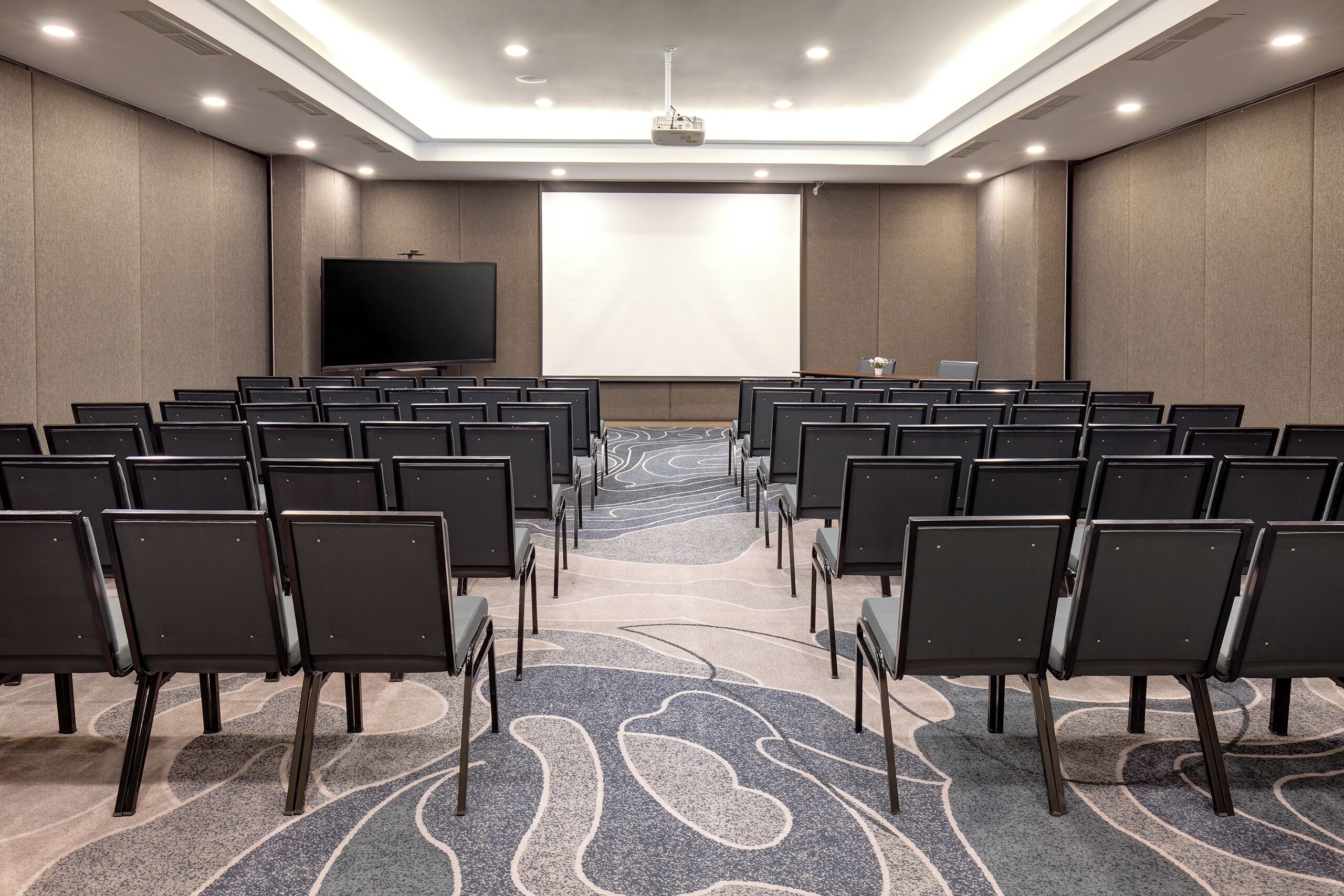 A conference room with rows of chairs facing a large screen.