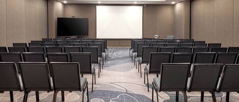 A conference room with rows of chairs facing a large screen.