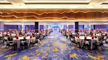 A banquet hall with round tables, chairs, and a carpeted floor.