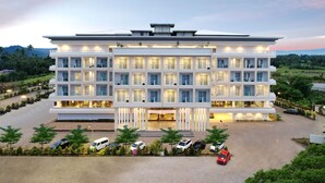 Un hotel moderno de varios pisos con un patio central, varios balcones y un estacionamiento.