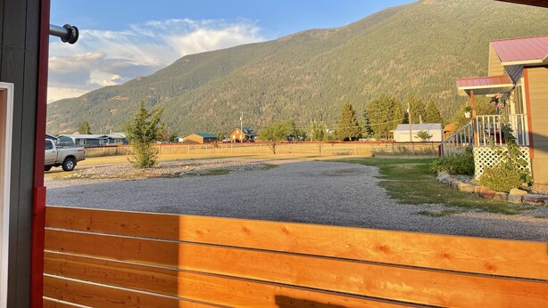 Uitzicht vanuit een houten raam op een landelijk landschap met bergen, een omheind gebied en een gebouw met een rood dak.