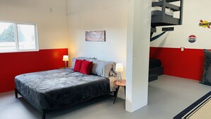 Een slaapkamer met een bed, twee bedlampen, een rode en witte muur, een raam, een schilderij, een trap en een Jeep logo op de muur.