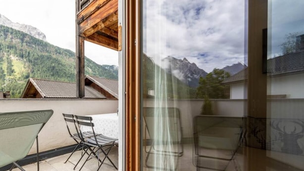 Un balcón con vistas a montañas, una puerta de cristal y mobiliario exterior.