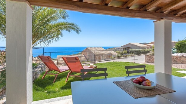 A covered outdoor seating area with a table and chairs, overlooking a coastal view with a clear sky. - Casa del Mare Blu - Seaview apartment with pool (Tertenia)