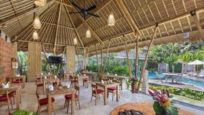 An indoor dining area with bamboo ceilings, wooden tables, and red cushioned chairs. - Kailash Suites Ubud (Sukawati)