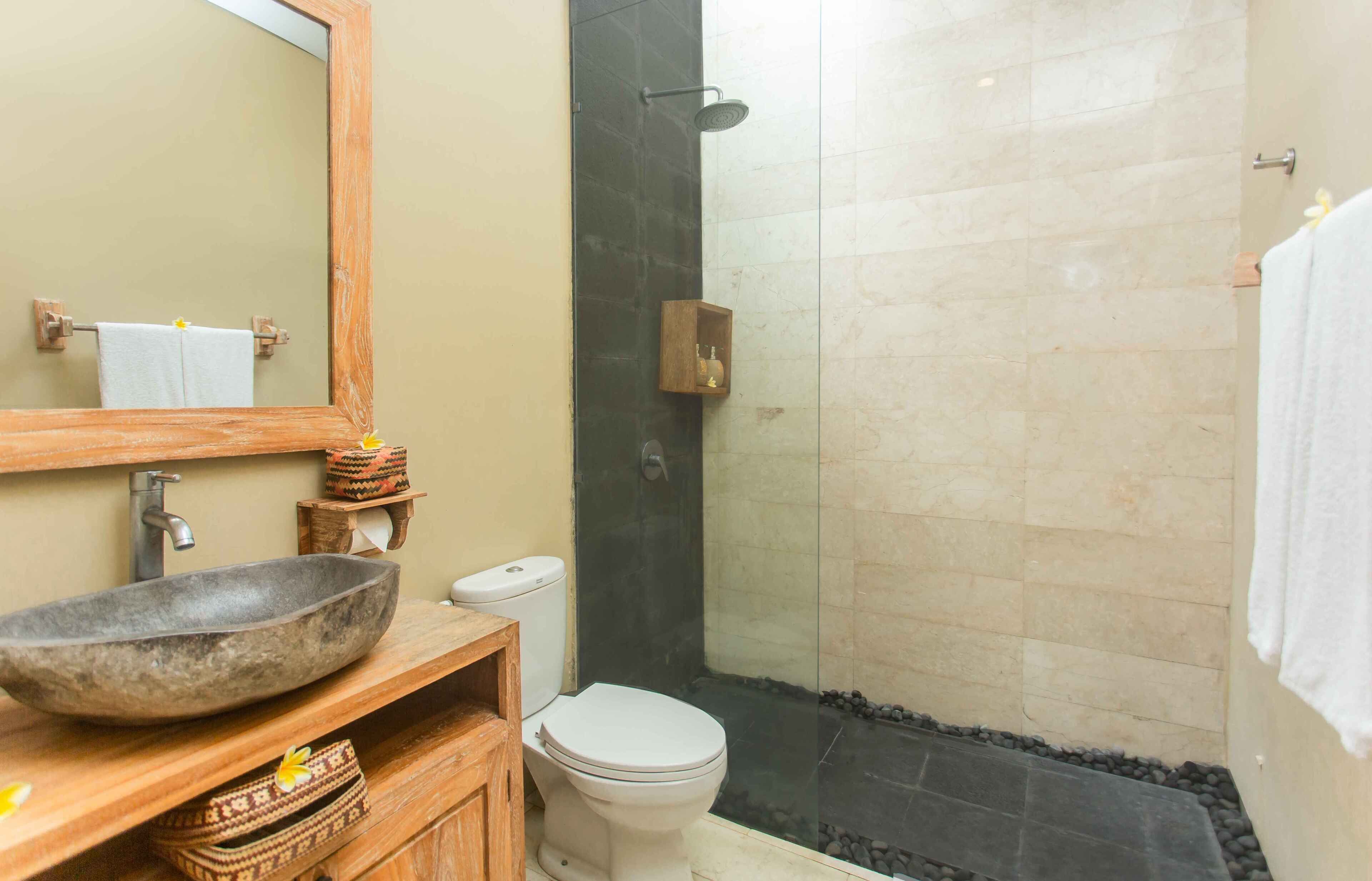 Une salle de bain dotée d’un grand miroir, d’un meuble-lavabo en bois, d’un lavabo en pierre, de toilettes et d’un espace douche.