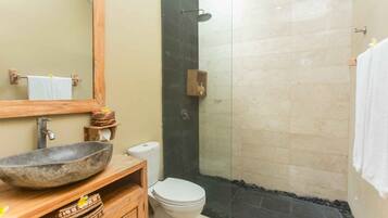 Une salle de bain dotée d’un grand miroir, d’un meuble-lavabo en bois, d’un lavabo en pierre, de toilettes et d’un espace douche.
