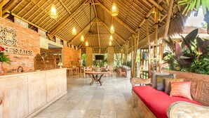 A spacious lobby with a high bamboo ceiling, a reception desk, a red sofa, and a dining area. - Kailash Suites Ubud (Sukawati)