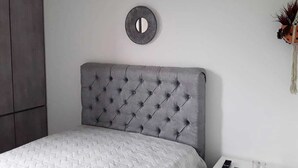 Un dormitorio con cabecera capitonada, un espejo redondo y una cama con colchón acolchado.