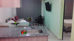 Una cocina compacta con encimera de granito, pileta de acero inoxidable y un pequeño comedor con una silla y una mesa.
