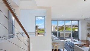 Un interior moderno con una escalera, un sofá, una mesa de centro y grandes ventanales que ofrecen vistas al exterior.