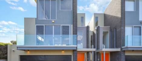 A modern two-story house with a garage, large windows, and a balcony.