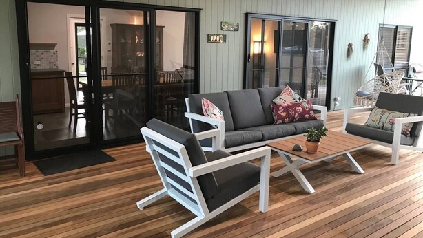 Ein geräumiges Zimmer mit Holzboden, einem grauen Sofa, zwei weißen Sesseln und einem kleinen Tisch mit einer Pflanze.