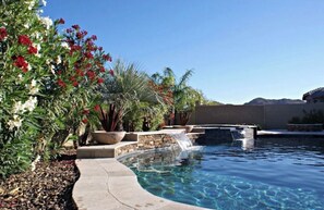 Une piscine agrémentée d’une cascade, entourée d’une végétation luxuriante et de plantes en fleurs.
