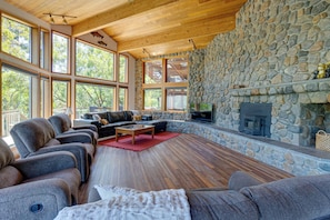 A spacious living room with a stone fireplace, large windows, and a cozy seating area.