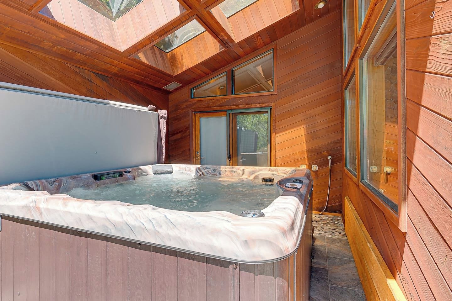 Een hottub in een houten chalet met een dakvenster erboven.