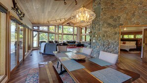 Un amplio espacio habitable con pared de piedra, techo de madera y grandes ventanales.