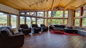 Un salón espacioso con techo de madera, ventanas amplias que ofrecen vistas a un paisaje boscoso y una pared de piedra.