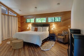 A bedroom with a large bed, two bedside lamps, a chair, a small rug, and a wooden floor.