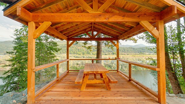 Un belvédère en bois avec une table de pique-nique, entouré d’une balustrade, d’où l’on a une vue sur un lac et des collines boisées.