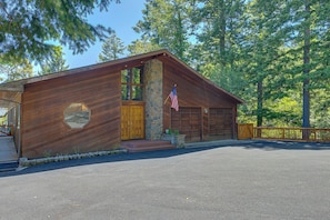 A wooden cabin with a stone foundation, a garage, and a flagpole with an American flag. - Rogue Keystone Lodge/Epic River Views/Sleeps 7/SPA (Gold Beach)