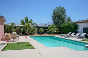 A swimming pool with lounge chairs, a small lawn area, and palm trees. - 4bd & Sleeps up to 10 - Saltwater Pool, Sunloungers, Mini Golf & Game Room (Indio)