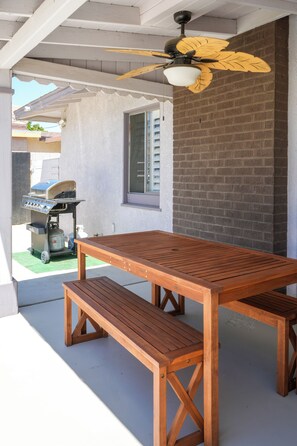 An outdoor patio with a wooden table and bench, a ceiling fan, and a barbecue grill. - 4bd & Sleeps up to 10 - Saltwater Pool, Sunloungers, Mini Golf & Game Room (Indio)