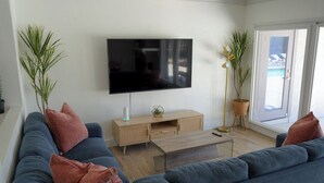 A modern living room with a large flat-screen TV, a wooden coffee table, and a blue sofa with red cushions. - 4bd & Sleeps up to 10 - Saltwater Pool, Sunloungers, Mini Golf & Game Room (Indio)